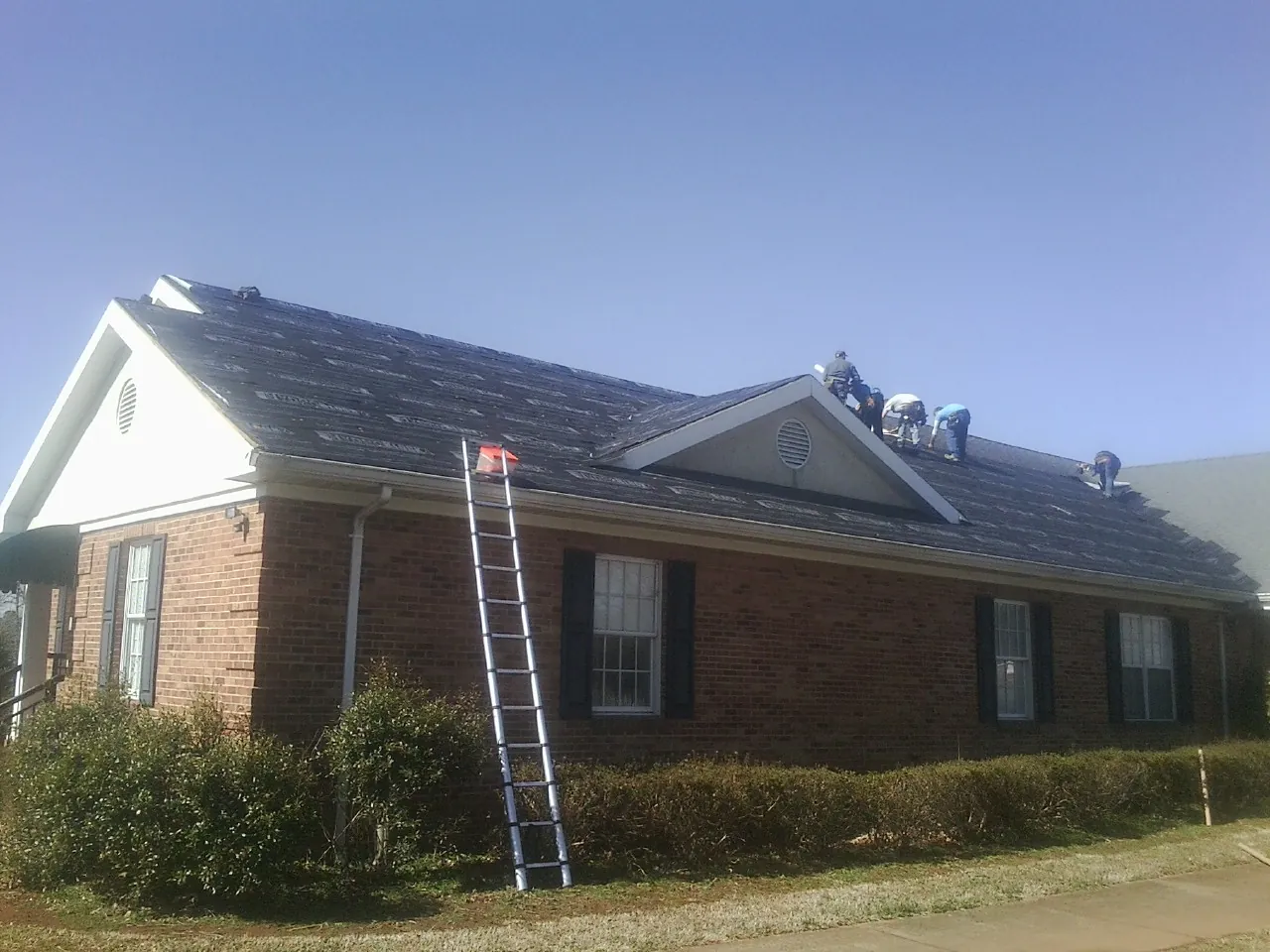 Crew tearing shingles off a brick ranch roof with a ladder set — Emergency Roof Repair work by our crew in Dedham