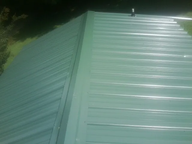 New green metal panels meeting at the ridge of a roof — Flat Roof Repair work by our crew in Dedham
